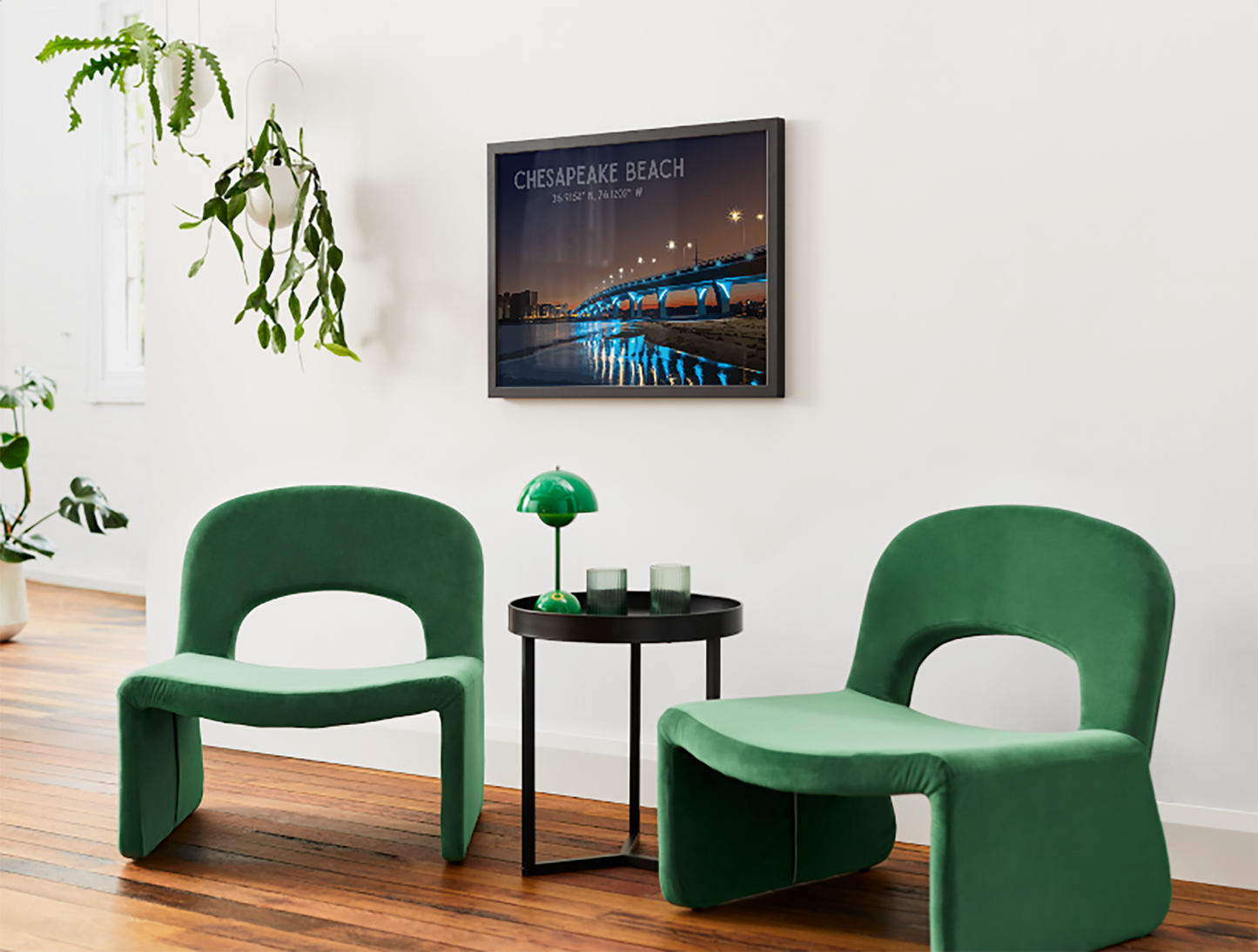 Two green chairs in a room with a framed picture of Chesapeake Beach on the wall.